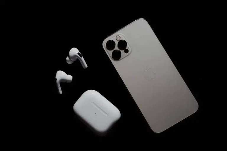 Close-up of smartphone and wireless earbuds on a dark surface, showcasing modern tech gadgets.