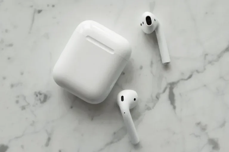 AirPods colorés : le jaune et le rose testés en 2016 refont surface Close-up of wireless earphones and charging case on a marble surface, showcasing modern technology.