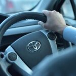 Close-up view of a hand gripping a Toyota steering wheel in a car interior, Faisalabad, Pakistan.