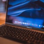 Close-up view of an open MacBook Pro with a dim blue screen in a cozy indoor setting.