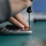 iFixit revient sur l'App Store le 9 décembre 2025 avec FixBot, mais la batterie fait doublon Detailed shot of smartphone repair with a screwdriver and hand close-up.