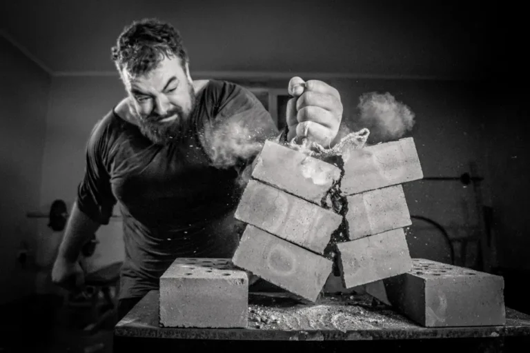 Dynamic image of a man smashing bricks with bare hands indoors.