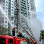 Incendie de Hong Kong : Tim Cook promet un don Apple sans montant Firefighters using hoses to extinguish flames on high-rise building exterior in an urban environment.