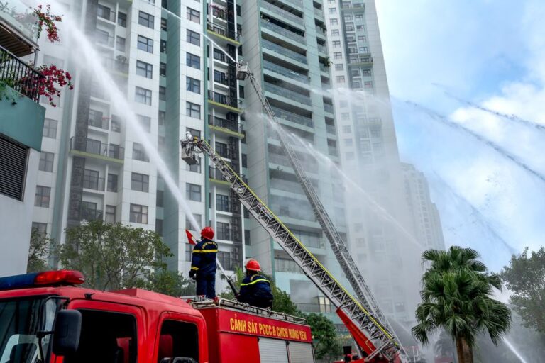 Incendie de Hong Kong : Tim Cook promet un don Apple sans montant Firefighters using hoses to extinguish flames on high-rise building exterior in an urban environment.