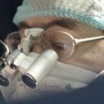 Focused surgeon wearing a surgical mask and loupes during an operation.