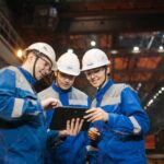 Group of engineers discussing project on a tablet in a factory setting.