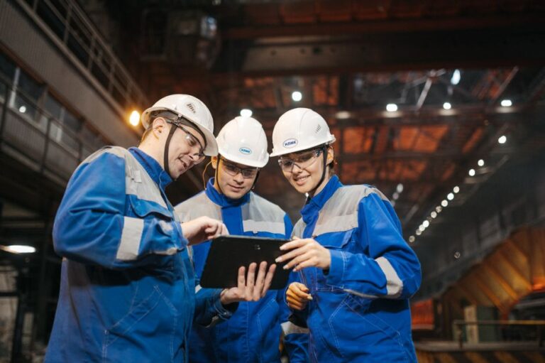 Apple quitte le showroom : la Manufacturing Academy sur le terrain Group of engineers discussing project on a tablet in a factory setting.