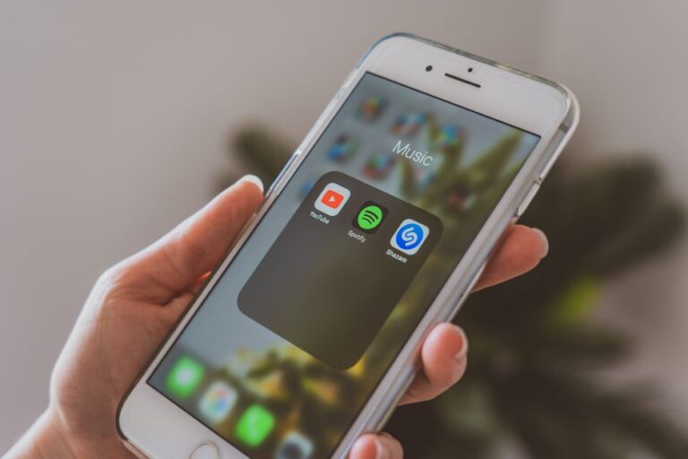 Apple Music Replay 2025 : retrouver ses tops sans jouer à cache-cache Hand holding a smartphone displaying popular music apps like Spotify and Shazam in a close-up shot.