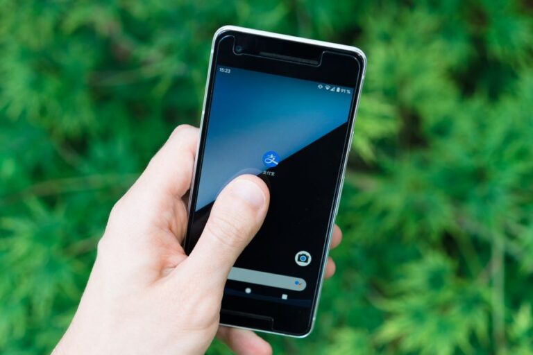Hand holding smartphone with app icon on screen, showcasing modern technology outdoors.