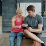 Apple Fitness+ s’étend à 28 marchés avec doublage IA et K-Pop Man and woman in gym wear reviewing training plan on tablet indoors.