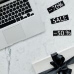MacBook Air à 599 dollars en janvier 2026 : le modèle compte Marble workspace with a laptop, gift box, and sale tags offering discounts.