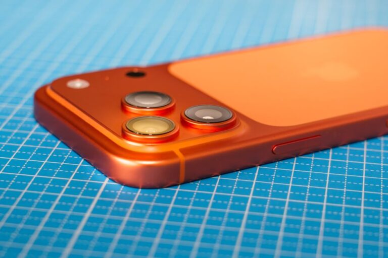 iPhone 17 Pro après trois mois : l’A19 Pro chauffe moins, mais iOS tousse Modern smartphone with a triple camera on a vibrant grid surface, showcasing advanced technology.