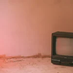 Old TV set with CRT screen on rough cement floor near wall in building