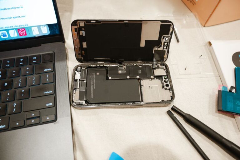 MacBook Pro M5 14 pouces : la batterie desserre l’étau Open iPhone with repair tools and laptop, showcasing DIY battery replacement process.
