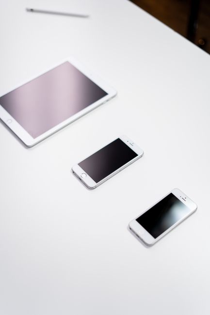 Overhead view of a digital tablet, smartphone, and stylus on a white surface.