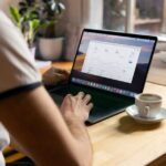 Microsoft Office 2024 à 99,97 $ : le piège du code Person working on a laptop with analytics in a cozy home office setting, coffee in hand.