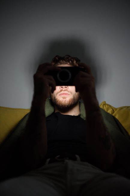 Portrait of a man with a beard capturing a photo on his smartphone in low light, highlighting the shadows.