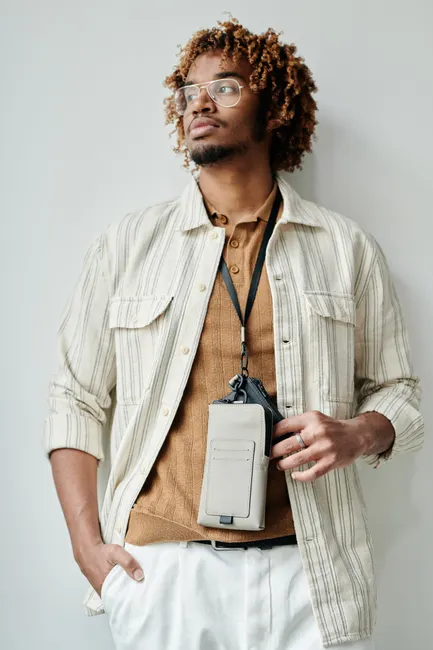 Portrait of a stylish black man in a modern outfit with eyeglasses and a phone pouch.