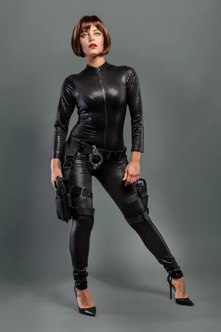 Portrait of a woman in a sleek black bodysuit with spy-themed accessories.