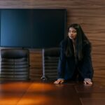 Professional woman in corporate attire standing in a sophisticated boardroom setting.