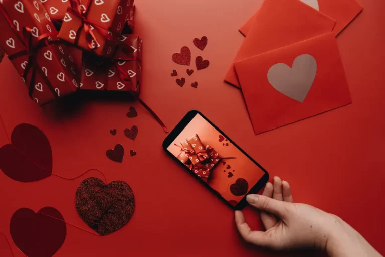 Romantic Valentine's Day scene featuring heart-themed gifts and a smartphone on a red background.