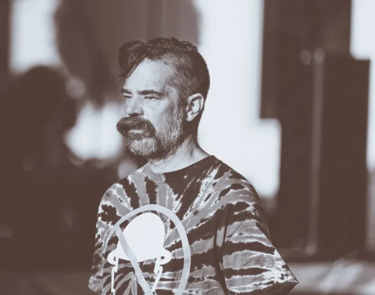 Alan Dye quitte Apple pour Meta le 31 décembre 2025: Liquid Glass change de pilote Sepia-toned portrait of a man with a beard wearing a tie-dye shirt outdoors during the day.