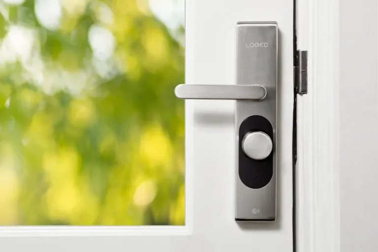 Doma Home prépare une porte intelligente, Apple garde les clés? Sleek smart door lock on a white door with blurred green foliage in the background.