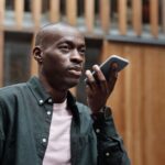 John Giannandrea quitte Apple au printemps 2026 : Siri change de pilote Stylish adult man using his smartphone for voice commands in an outdoor urban setting.