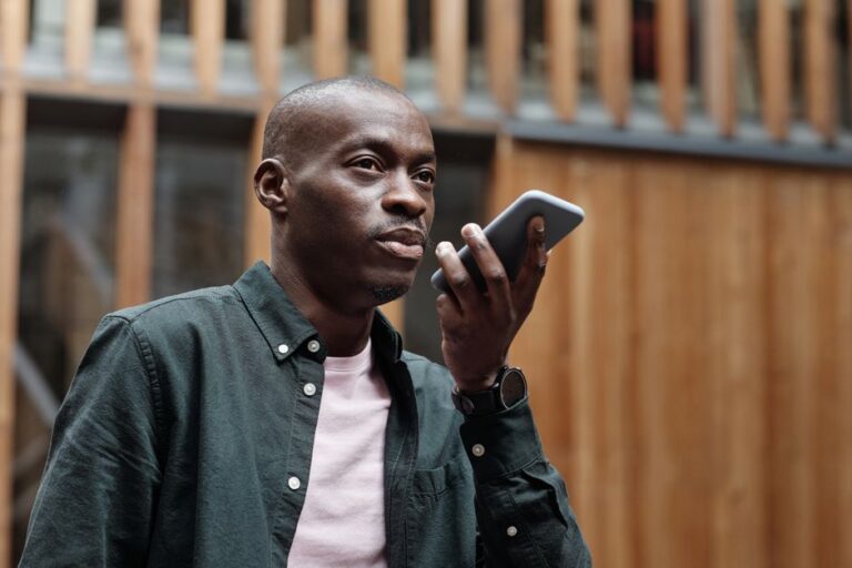 John Giannandrea quitte Apple au printemps 2026 : Siri change de pilote Stylish adult man using his smartphone for voice commands in an outdoor urban setting.