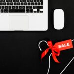 MacBook Air en promo fin 2025 : M4 à 749,99 $, M1 à 499 $ Stylish flat lay of a laptop, mouse, and sale tag on a hanger for online shopping concept.