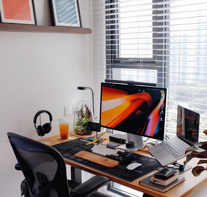 Deux claviers et un Mac mini M1 : le bureau Apple qui tient encore en 2025 Stylish home office with dual screens, laptop, and tech gadgets by a bright window for optimal productivity.