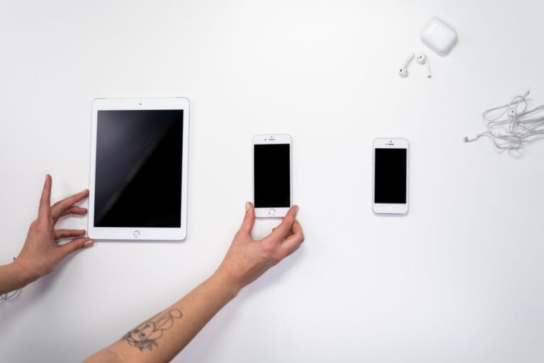 Apple 2027 : six ou sept iPhone par an, le catalogue se complique Top view of hands arranging an iPad, iPhones, and earphones on a white surface. Perfect for tech-related imagery.