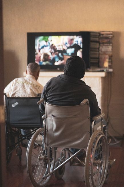 Two adults in wheelchairs watching television, creating a cozy and inclusive atmosphere indoors.