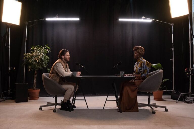 The Rest Is History remporte Apple Podcasts 2025, une première britannique Two hosts recording a podcast in a well-lit studio setup with microphones and studio lights.
