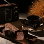 Warm rustic scene with chocolate wafers, a cup of coffee, and vintage radio on wooden table.