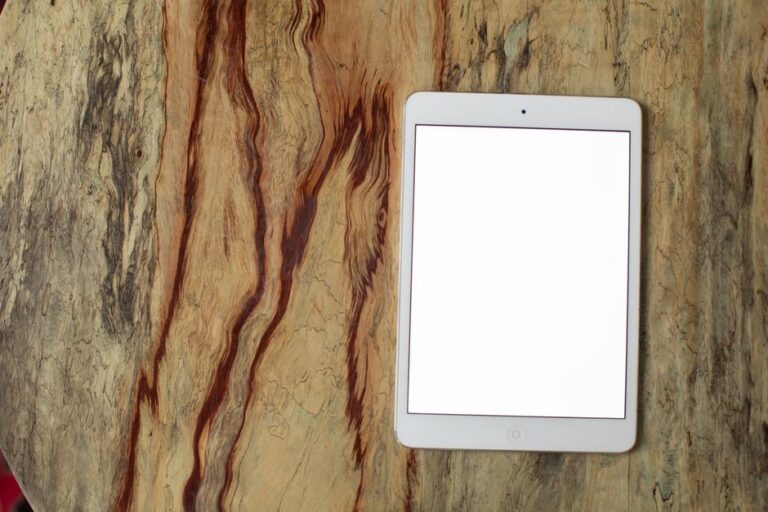 iPad mini 8 : A20 Pro, OLED et sortie visée fin 2026, le 60 Hz en embuscade White tablet with blank screen placed on a textured wooden surface, viewed from above.
