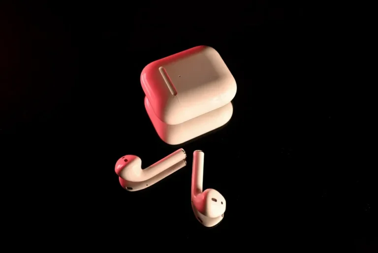 AirPods Pro 2 : 86,5 % des seuils à 10 dB près, sans miracle White wireless earbuds with a charging case, highlighted with red lighting on a reflective black surface.