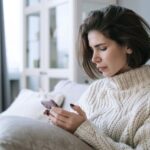 iPhone Pocket : Amazon tricote déjà des copies à 29,99 dollars Woman in knitted sweater using smartphone on a cozy sofa indoors.