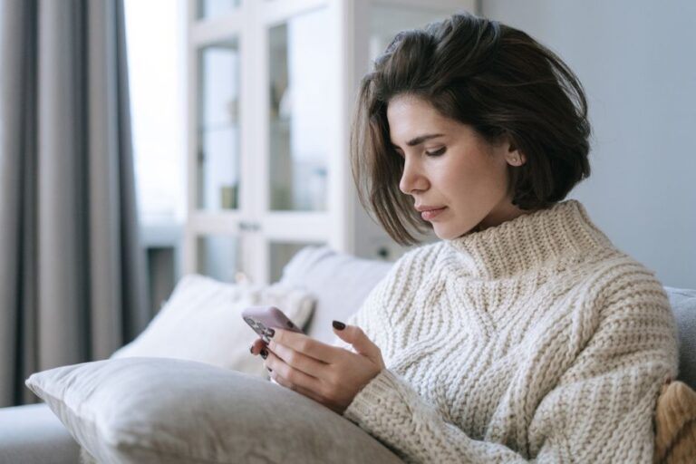 iPhone Pocket : Amazon tricote déjà des copies à 29,99 dollars Woman in knitted sweater using smartphone on a cozy sofa indoors.
