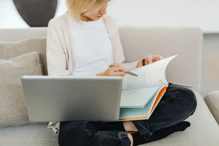 Babbel à 129,99 $ au Black Friday 2025 : le plan sans abonnement Woman sitting cross-legged on sofa, studying with a textbook and laptop, creating a cozy learning environment.