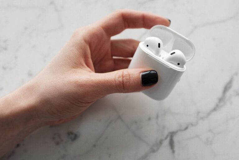 AirPods : Apple étudie des gestes par antenne, sans date annoncée A close-up view of a hand holding white wireless earbuds in a case on a marble surface.