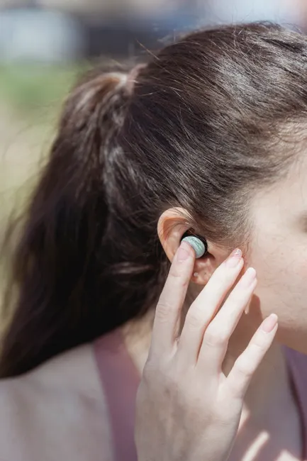 A detail shot of a woman adjusting a wireless earbud on a sunny day outdoors.