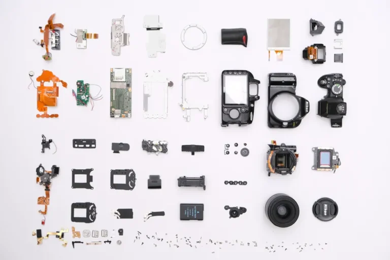 AirTag 2 démonté : 50 % plus sonore, la colle s’invite A detailed flat lay of disassembled camera components showcasing intricate electronics.