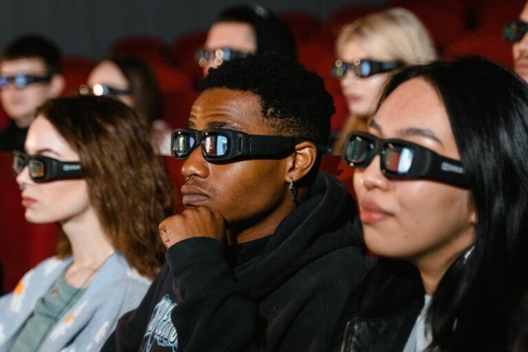 Xreal 1S à 449 dollars : le grand écran tient sur le nez A diverse group of adults wearing 3D glasses are watching a movie in a cinema theater.