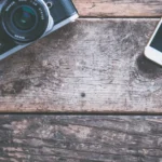 A flat lay of a vintage camera and smartphone on a rustic wooden table, ideal for tech and photography themes.