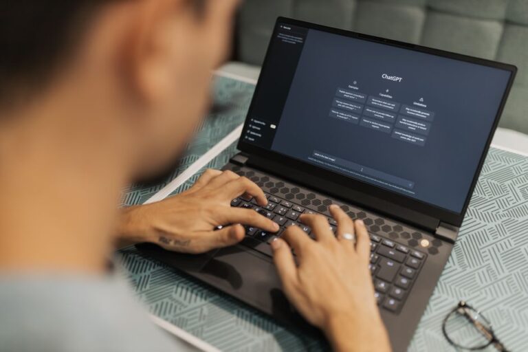 Apple Intelligence en 2026 : Siri, le Pin IA et l’iPhone 18 Pro dans le flou A focused individual types on a laptop running AI software indoors.