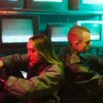 Criminal Record saison 2 arrive le 22 avril 2026, Londres voit rouge A futuristic scene capturing two individuals in a cyberpunk setting surrounded by televisions.