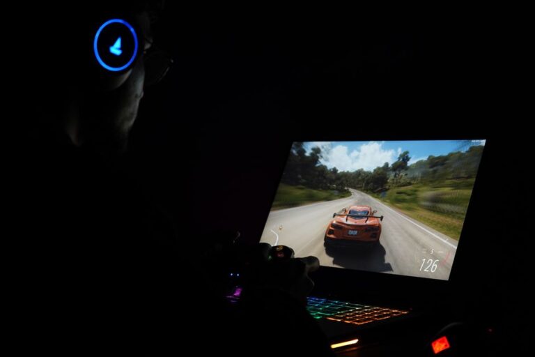 Apple en Formule 1 dès 2026 : le streaming ne fera pas tout A gamer using a laptop and headphones to play a car racing game in a dark setting.