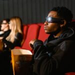 A group of adults in a cinema wearing 3D glasses watching a movie and eating popcorn.
