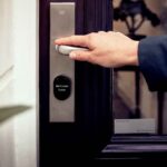SwitchBot au CES 2026 : serrures 3D, robot et lampe A hand opening a smart home door with digital access panel, conveying security and technology.